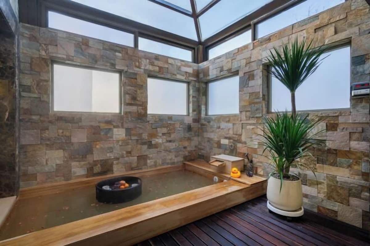 Um quarto de spa com paredes de pedra, um banco de madeira, uma banheira de hidromassagem e um vaso com planta.