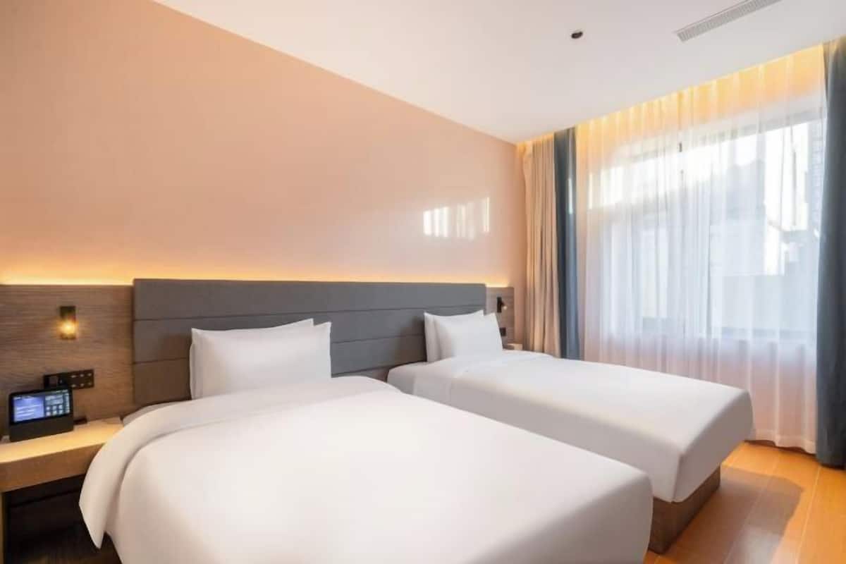 Quarto de hotel com duas camas, uma mesa de cabeceira com telefone e uma janela grande com cortinas.