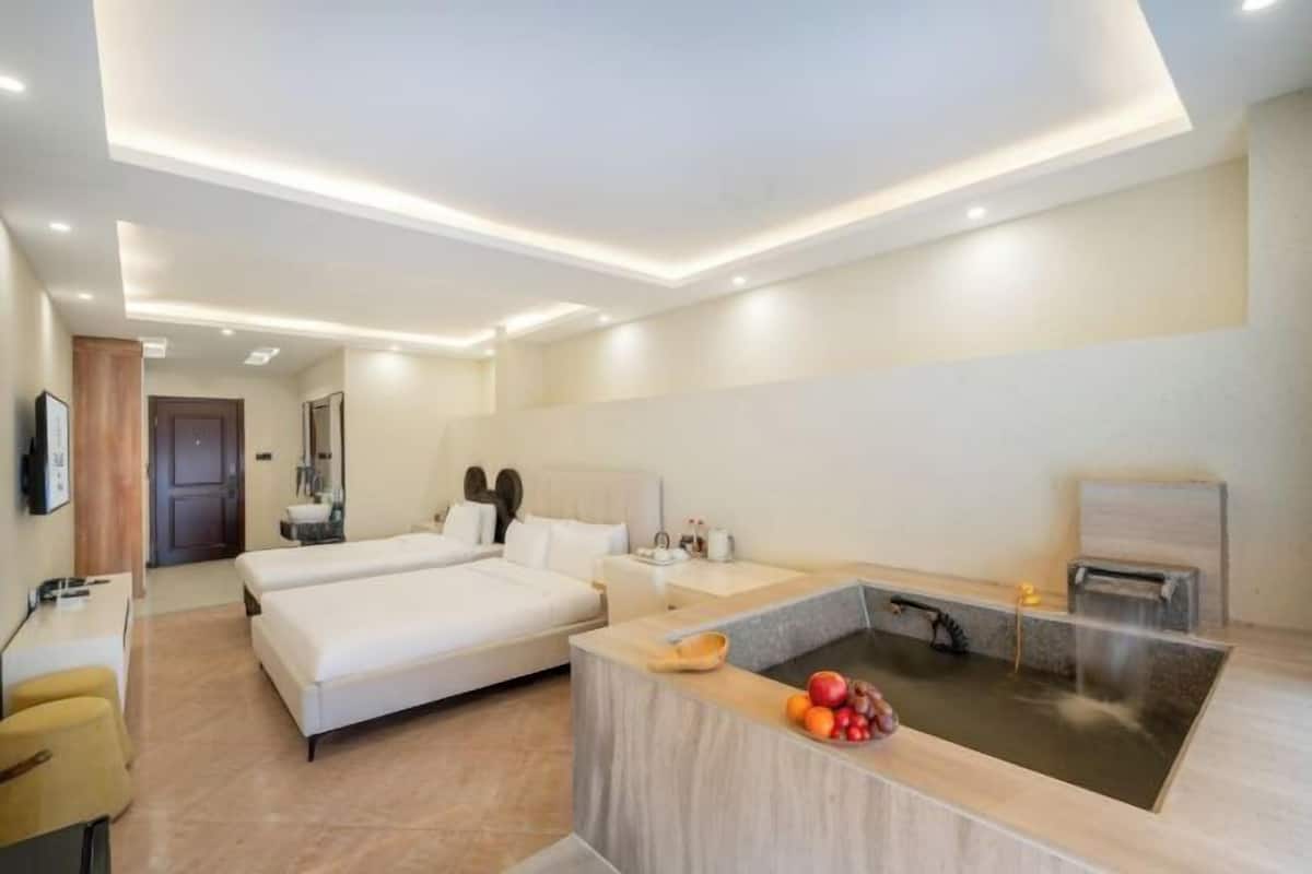 Quarto de hotel moderno com uma cama grande, uma pequena mesa de escritório, um elemento decorativo com água e uma área de chuveiro separada.
