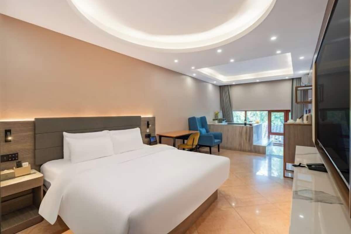 Quarto de hotel moderno com uma cama grande, uma mesa, uma cadeira, uma televisão e uma varanda com vista.
