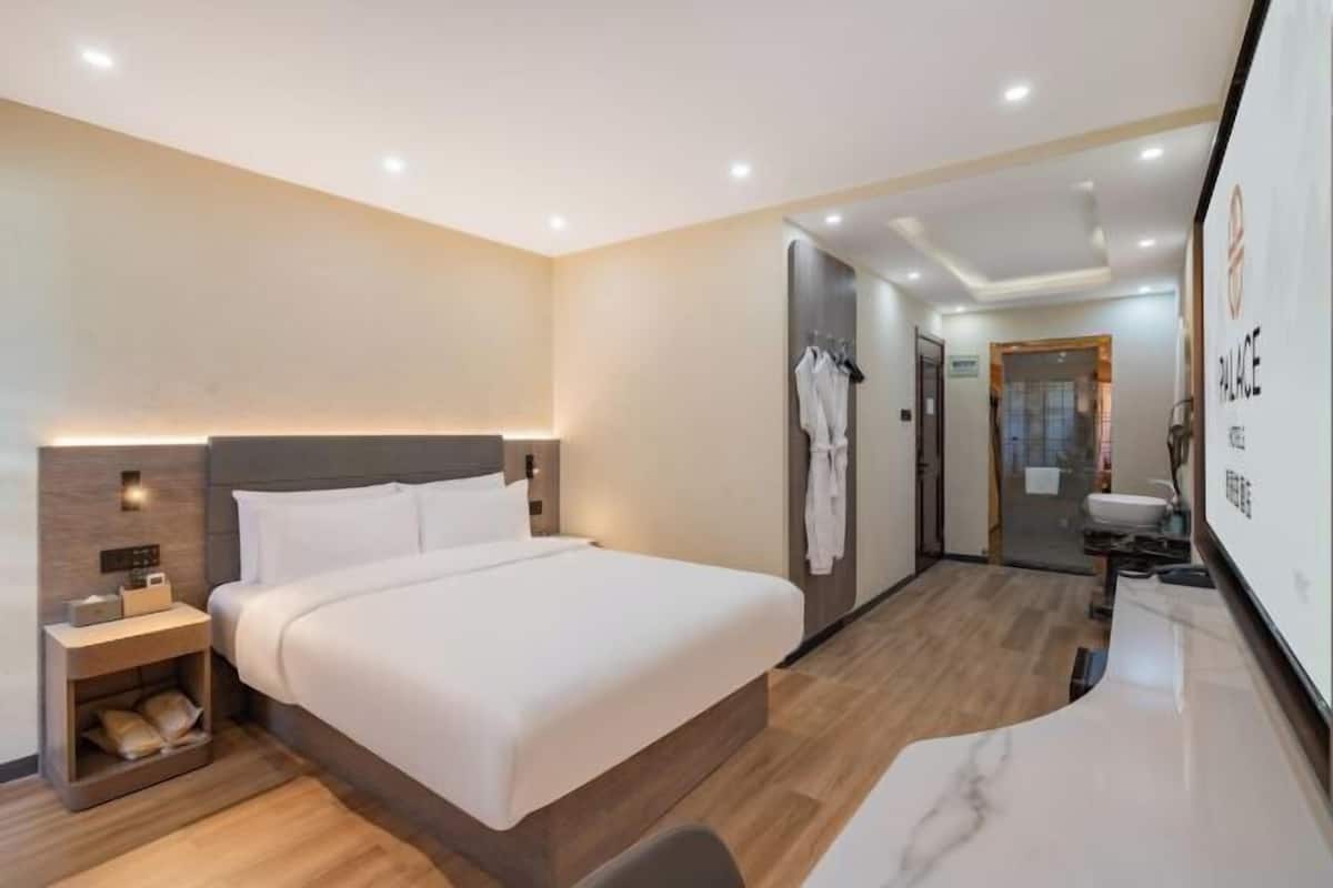 Quarto de hotel moderno com uma cama grande, mesa de cabeceira e banheiro visível através de uma porta aberta.