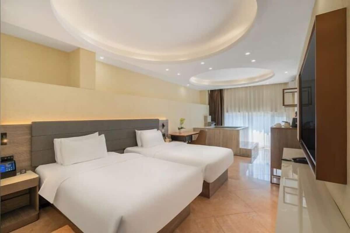 Quarto de hotel com duas camas, uma escrivaninha, televisão e banheiro.