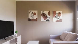 Una sala de estar moderna con un televisor de pantalla plana, una mesa de centro blanca, un sofá color beige y arte abstracto en la pared.