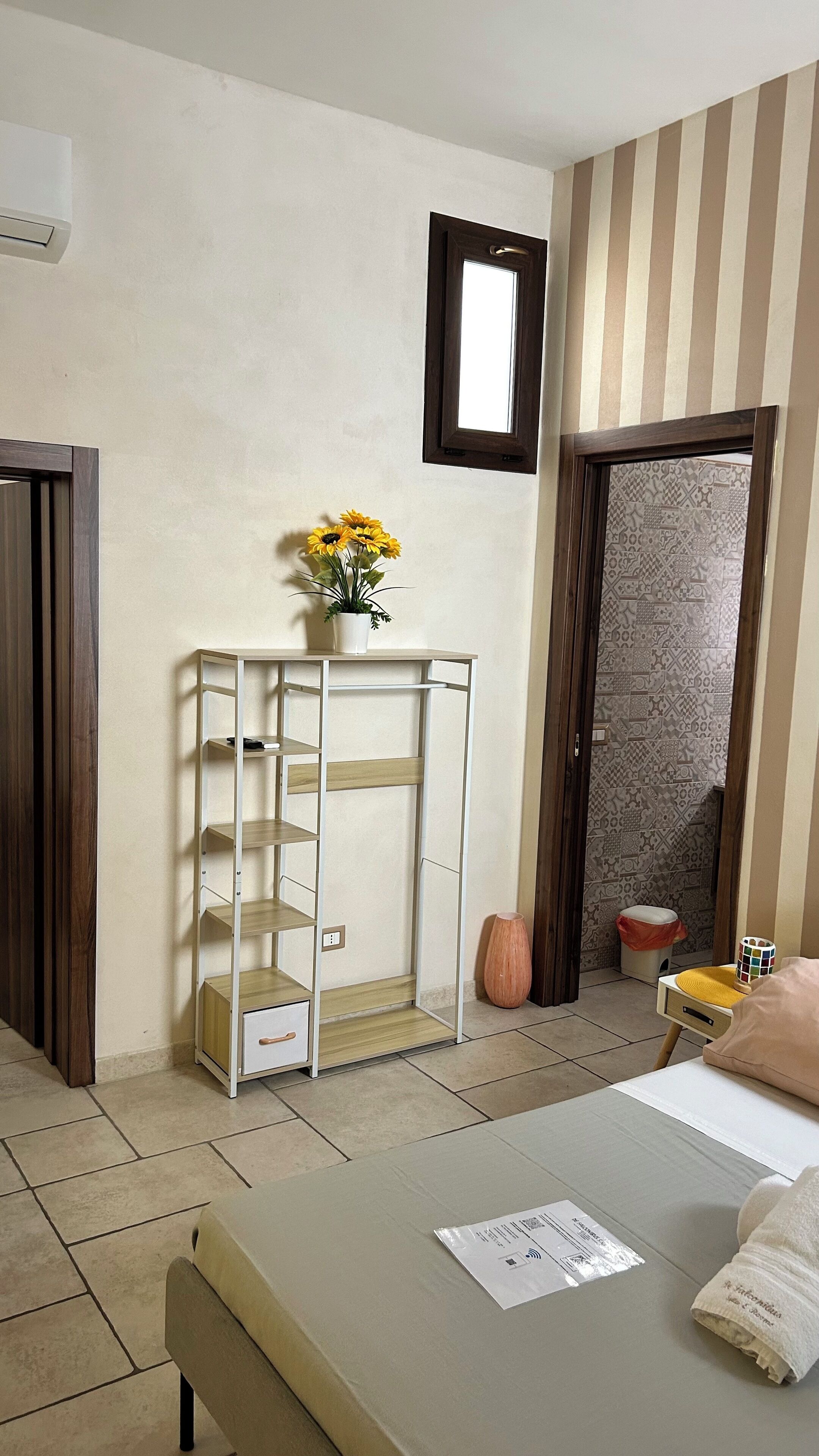 Een hotelkamer met een bed, een klein tafeltje met een bloevas, een wandplank en een kamer met een patroon op de muur.