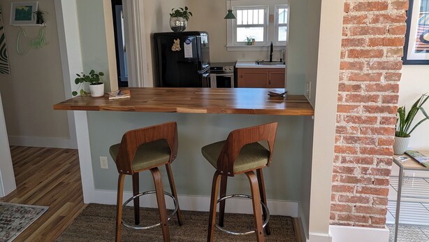 Een moderne keuken met een houten kookeiland, twee barkrukken en een accentmuur van baksteen.