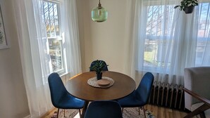 Een eetruimte met een ronde tafel, blauwe stoelen, een hangplant en een kamerbreed tapijt.