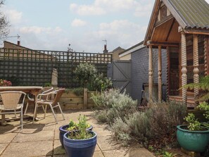A patio area with wicker chairs, a wooden table, and potted plants. - The Orchard Close Art House (Bury St Edmunds)
