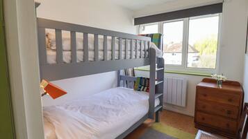 A bunk bed with a lower bunk, a wooden dresser, a chair, and a window with a view of greenery.