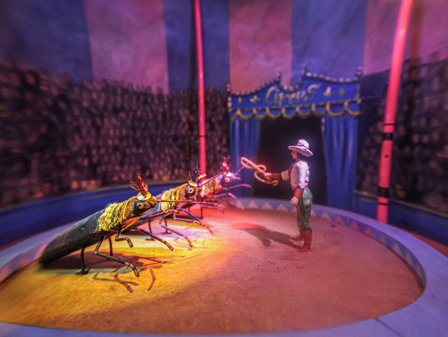 A circus scene with performers and an ant-like creature on stage.