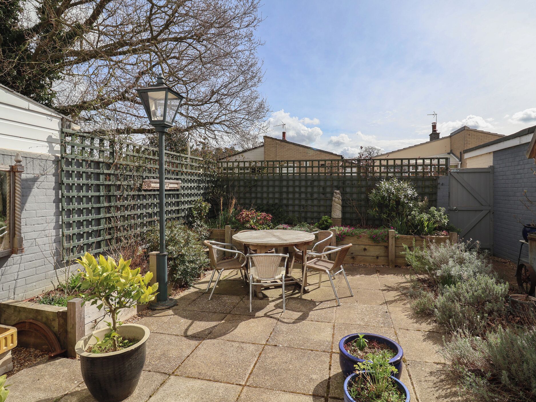 A patio area with a round table and chairs, surrounded by potted plants and a wooden fence.