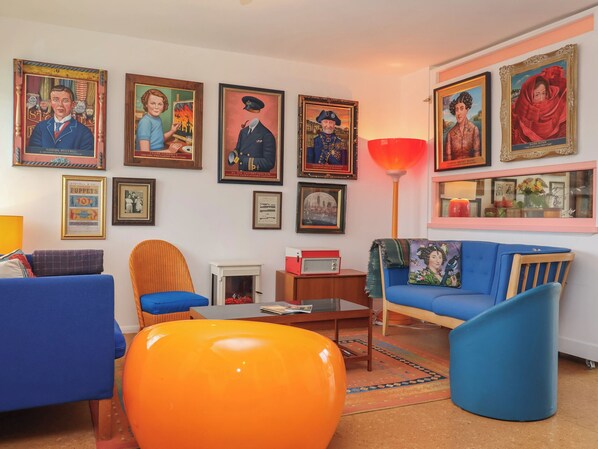 A living room with blue and orange furniture, a red lamp, and various framed pictures on the wall. - The Orchard Close Art House (Bury St Edmunds)
