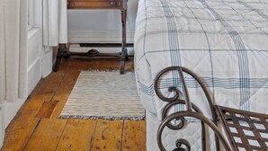 A bedroom with a bed, a bedside table with a lamp, a painting of a beach scene, and a wooden floor. - Historic Flat Best DT Location (Halifax)