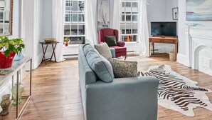 A modern living room with a grey sofa, a red armchair, a flat-screen TV, and a fireplace. - Historic Flat Best DT Location (Halifax)