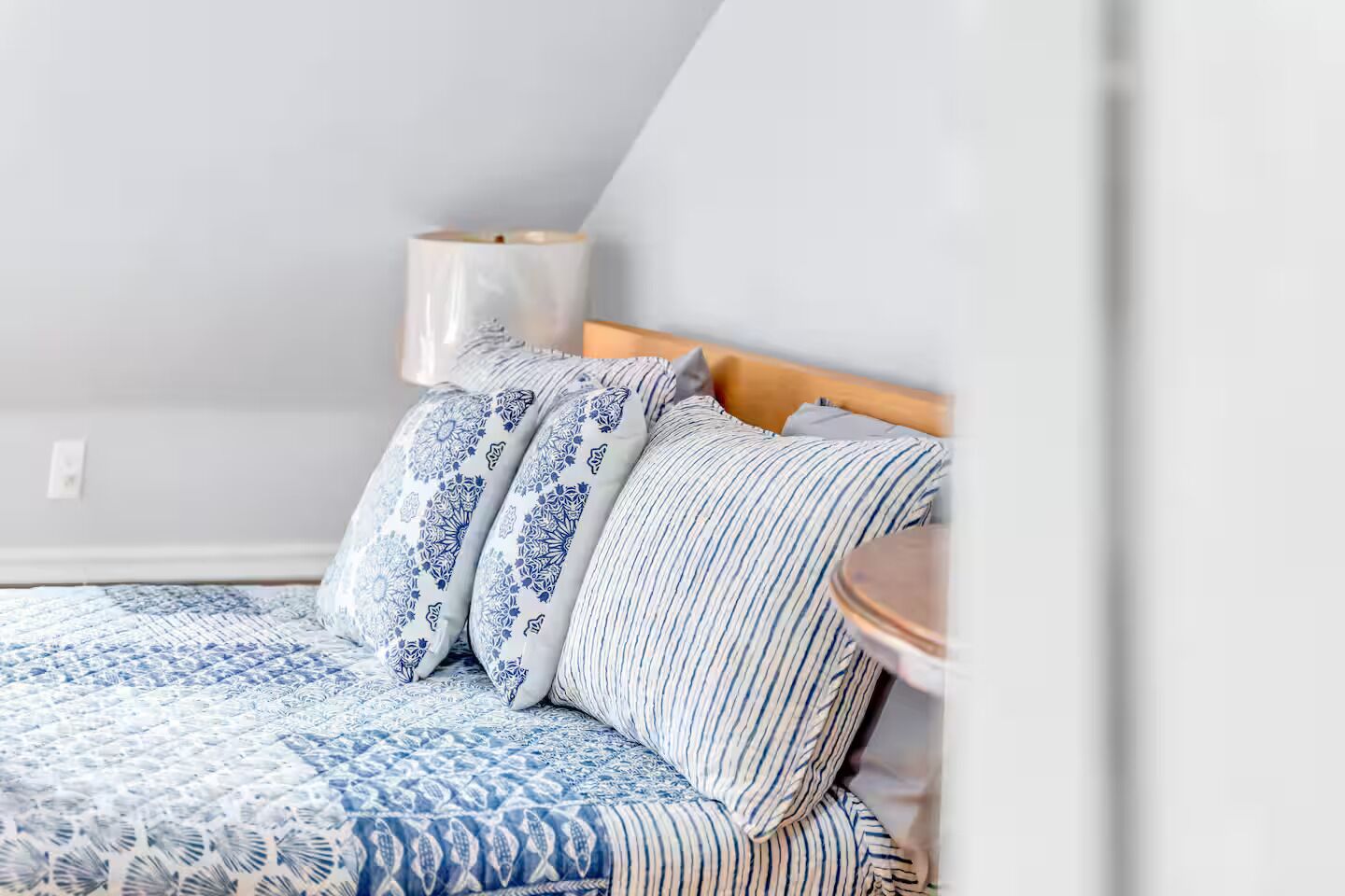 Une chambre à coucher avec un lit, des oreillers, une table de chevet et une lampe.