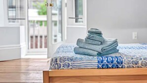 A neatly made bed with a patterned bedspread and a stack of folded towels on the side.