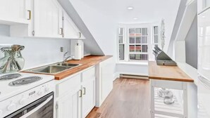 A modern kitchen with white cabinetry, a wooden countertop, and a built-in stove.