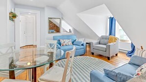 A modern loft apartment with a glass dining table, blue and grey sofas, and a brick wall accent.