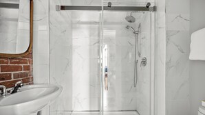 Un bagno moderno con cabina doccia in vetro, lavandino bianco e parete rivestita in marmo.