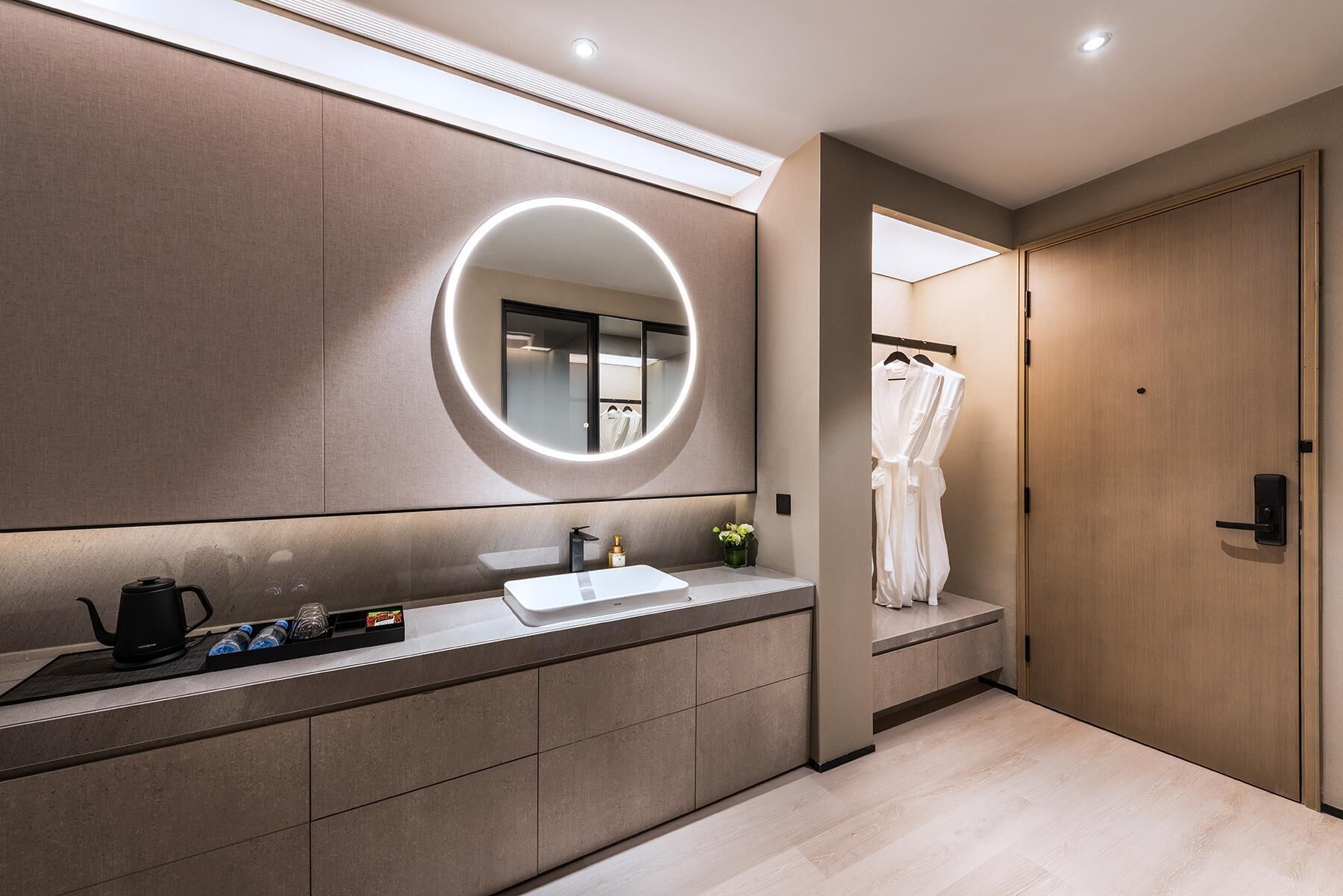 A modern bathroom with a large mirror, a sink, and a robe hanging on a door.