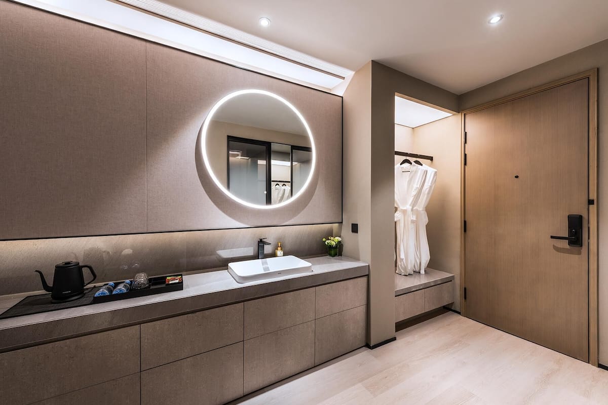 A modern bathroom with a large mirror, a sink, and a robe hanging on a door.
