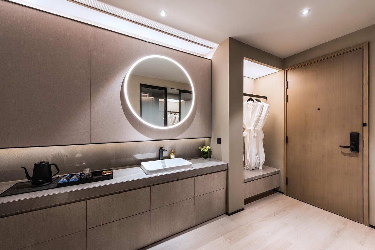 A modern bathroom with a large mirror, a sink, and a robe hanging on a door.