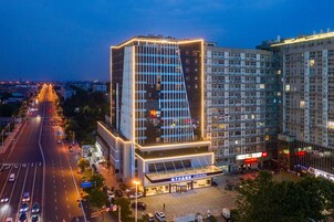 Un hotel moderno con una fachada de vidrio destacada, un área de entrada amplia y un estacionamiento.