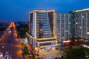 A modern hotel with a prominent glass facade, a spacious entrance area, and a parking lot.