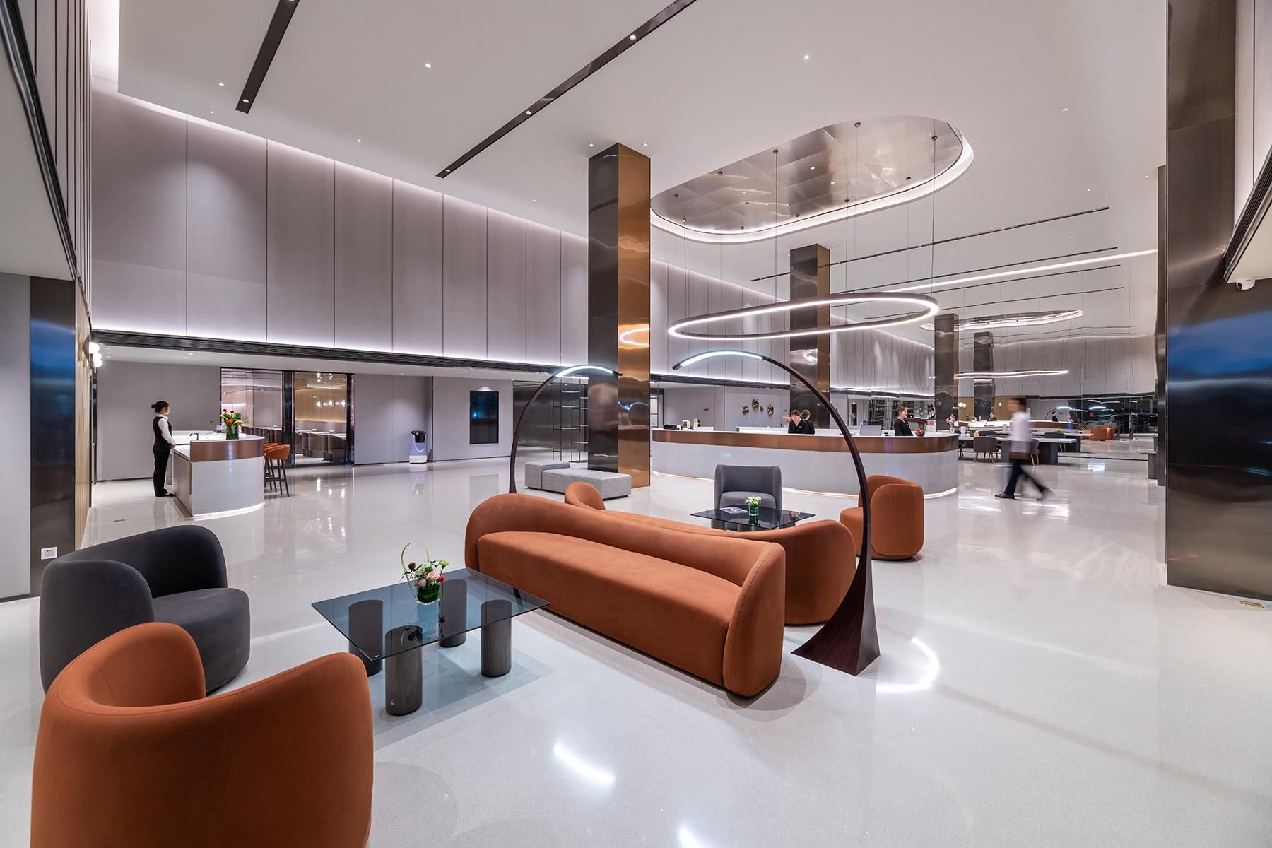 A modern lobby with a reception desk, seating area, and a kitchen in the background.