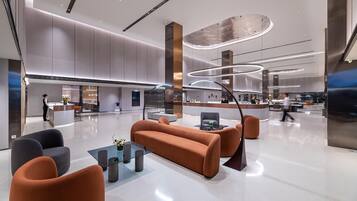A modern lobby with a reception desk, seating area, and a kitchen in the background.
