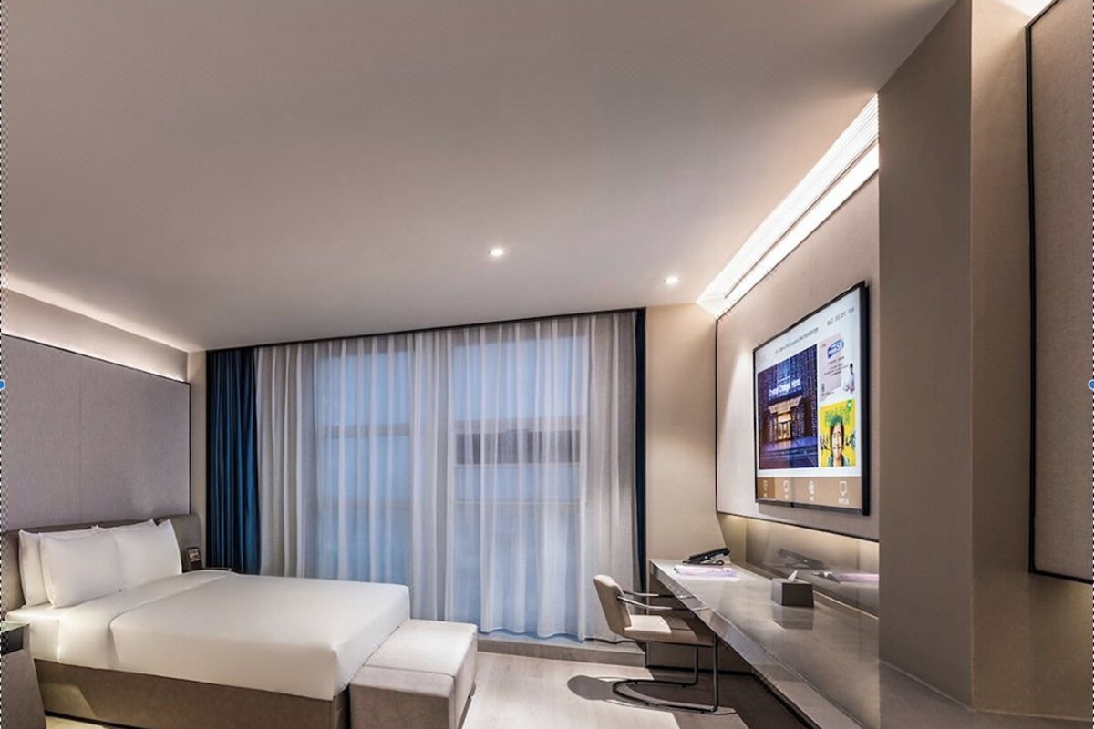 A modern hotel room with a large bed, a desk, a TV, and a window with curtains.
