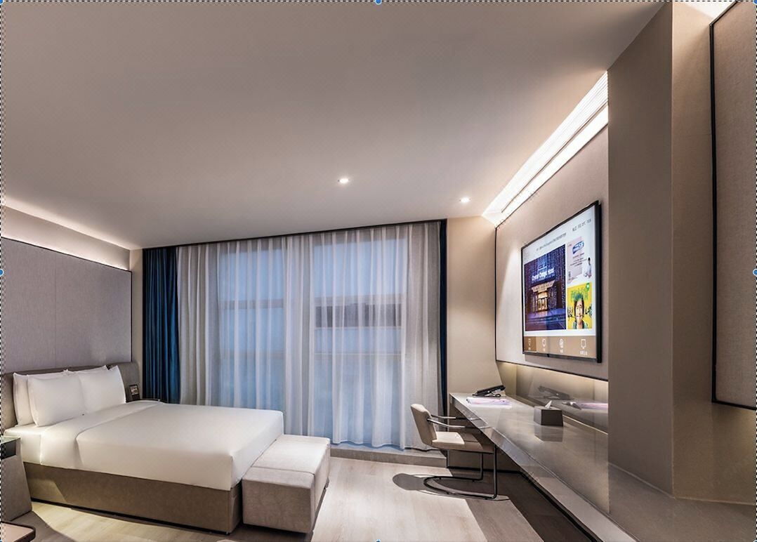 A modern hotel room with a large bed, a desk, a TV, and a window with curtains.