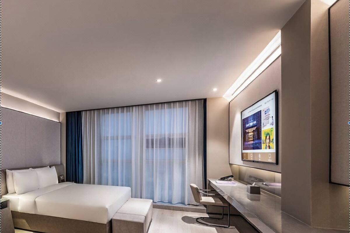 A modern hotel room with a large bed, a desk, a TV, and a window with curtains.