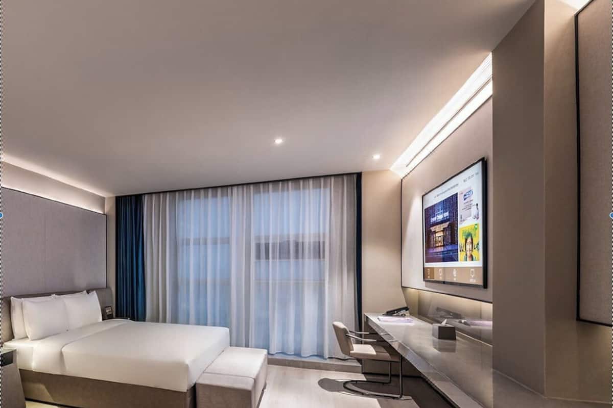 Une chambre d’hôtel moderne équipée d’un grand lit, d’un bureau, d’une télévision et d’une fenêtre avec des rideaux.