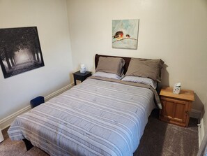 A neatly made bed with a striped comforter, a nightstand with a tissue box, and a painting of birds on the wall.