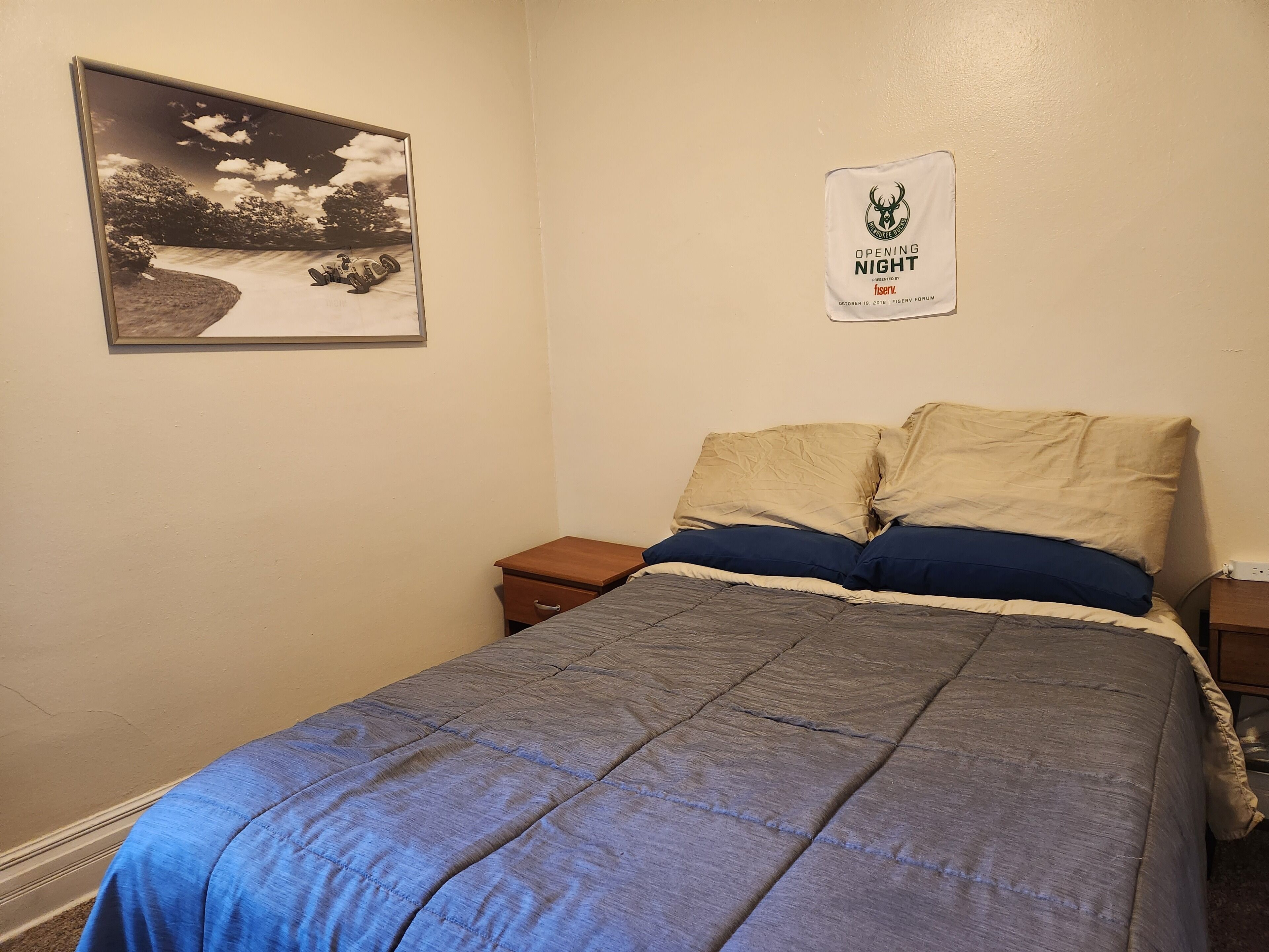 Ein Schlafzimmer mit Bett, Nachttisch, gerahmtem Bild und einem Poster an der Wand.