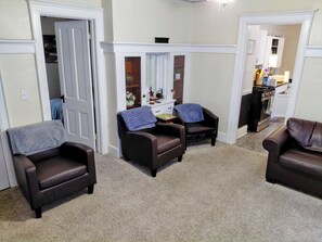 A living room with two leather armchairs, a small table, a mirror, and a doorway leading to another room.