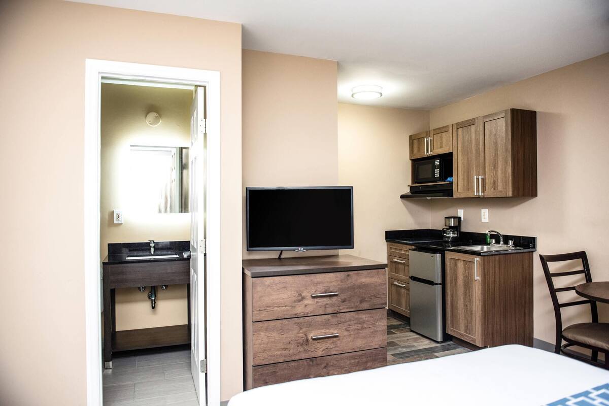 Quarto de hotel compacto com cozinha compacta, televisão de tela plana, cama e banheiro com espelho e pia.