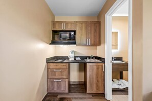 A compact kitchen with wooden cabinets, a microwave, a coffee maker, and a sink. - Suburban Studios Charlotte - Ballantyne (Charlotte)
