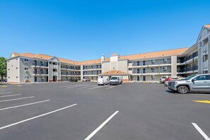 A multi-story hotel with a parking lot, several vehicles, and a clear blue sky. - Suburban Studios Charlotte - Ballantyne (Charlotte)