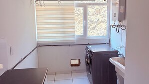 A compact laundry room with a washing machine, a drying rack, and a small sink.