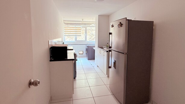 A narrow kitchen with a refrigerator, washing machine, and a small countertop.