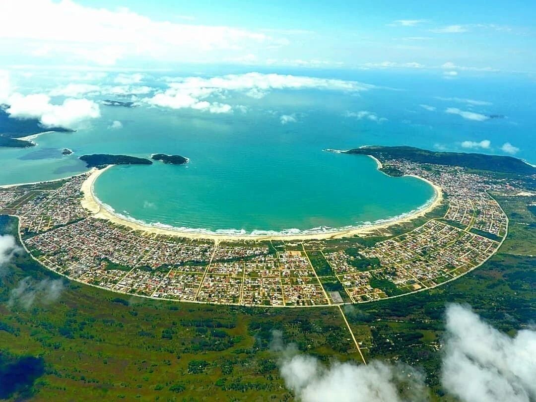 Vista aerea di una città costiera con disposizione circolare, spiaggia e corpi idrici circostanti.