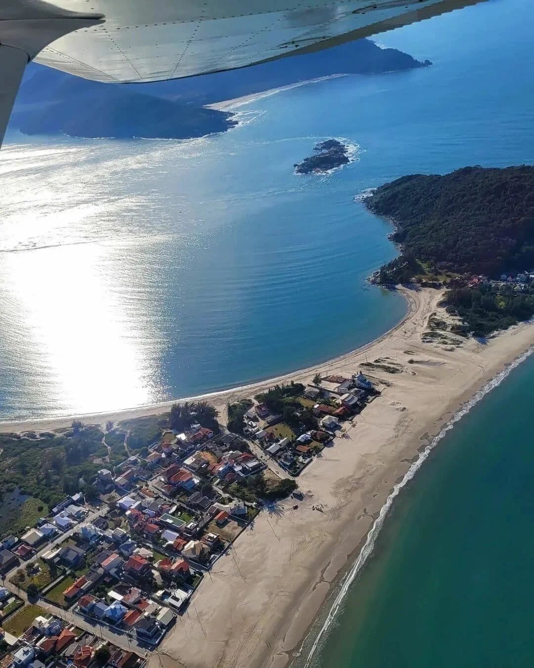 Luftaufnahme einer Küstenlandschaft mit Strand, Wohnhäusern und einer kleinen Insel.
