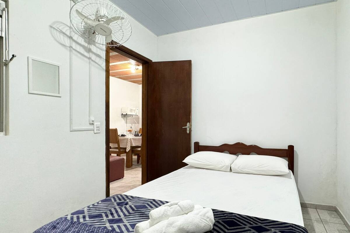 Ein Schlafzimmer mit Bett, Nachttisch, Stuhl und Ventilator.