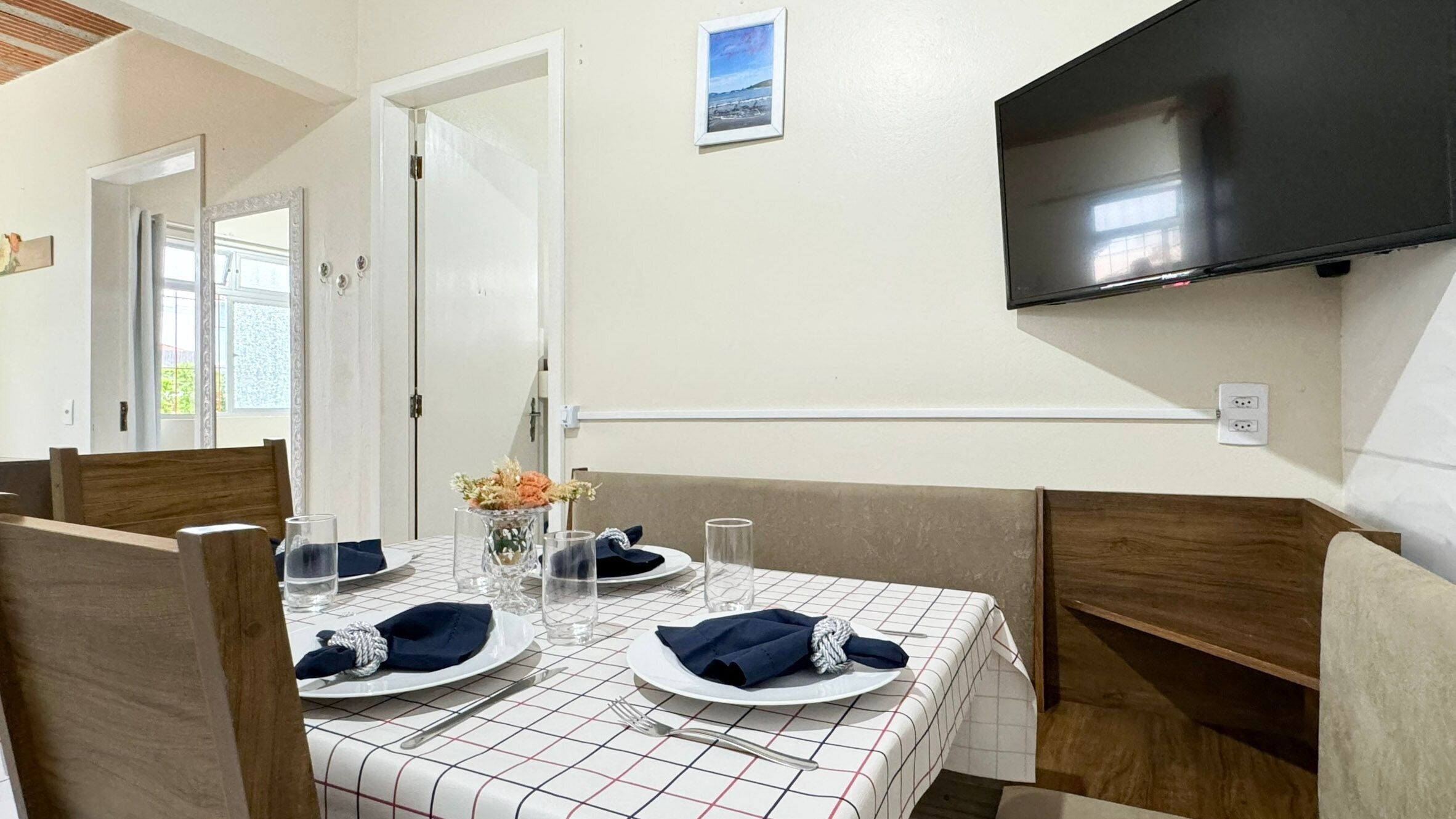 A dining area with a table set for two, a television mounted on the wall, and a door leading to another room.