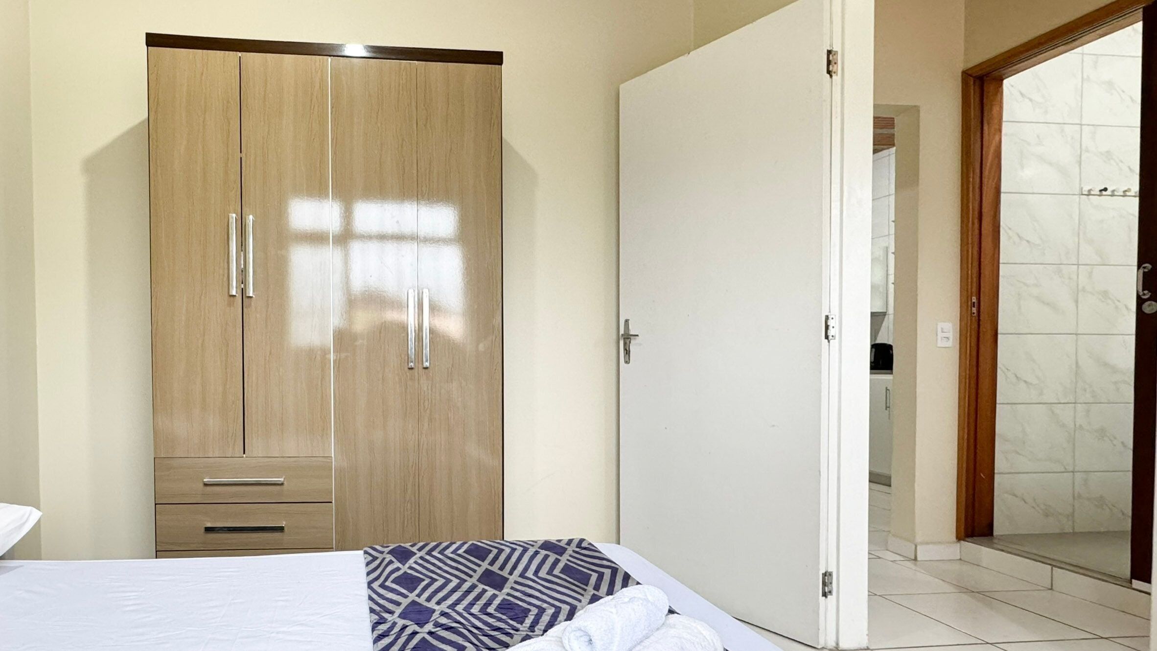 A hotel room with a large wardrobe, a bed with a patterned bedspread, and a bathroom visible through an open door.