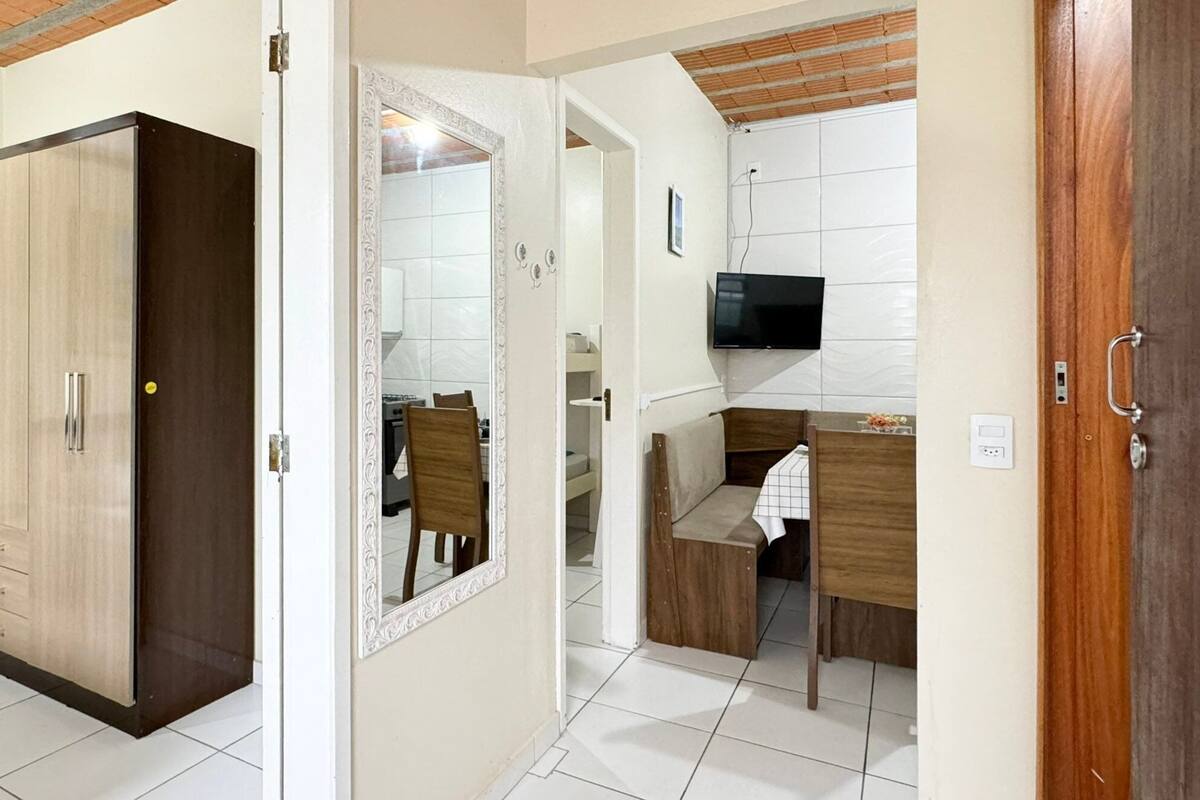 Ein kleines Zimmer mit Kleiderschrank, Spiegel, Essbereich und Wandfernseher.