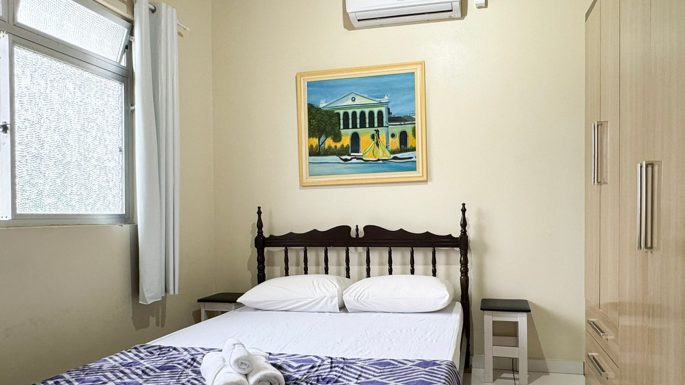 Ein Schlafzimmer mit einem Bett, einem Bild eines Gebäudes, einem Fenster und einer Klimaanlage.