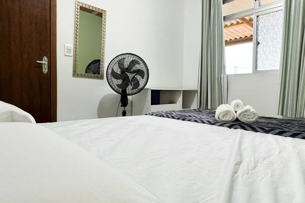 Ein Hotelzimmer mit Bett, Standventilator, Spiegel und einem Fenster mit Vorhängen.