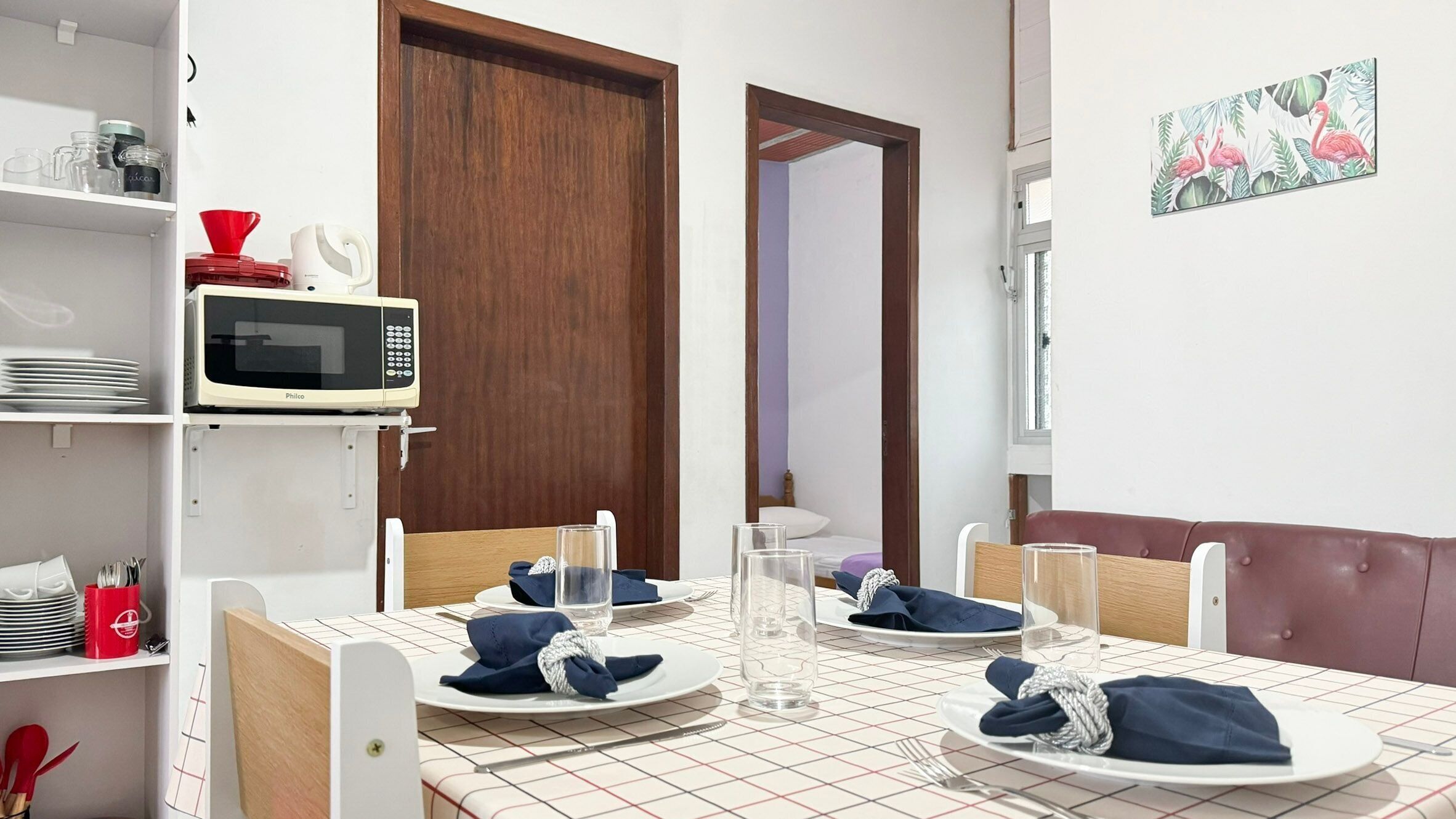 A neatly set dining table with plates, glasses, and cutlery, a microwave above it, and a wooden door in the background.